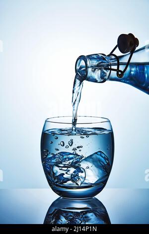 Bottle of fresh water pouring water in a glass with ice cubes Stock Photo