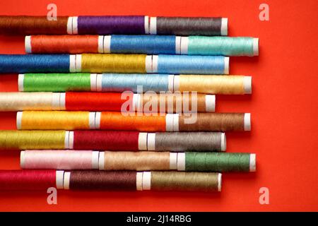 spools of colored thread lie in horizontal rows on a red background Stock Photo