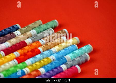 on a red background, there are spools of colored thread in the lower left corner diagonallyon a red background, there are spools of colored thread in Stock Photo