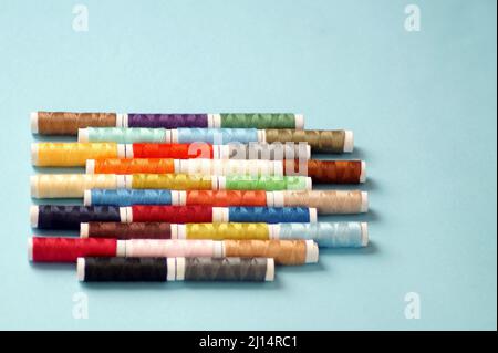 spools of colored thread lie in horizontal rows on a blue background Stock Photo