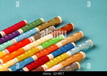on a blue background lie diagonally spools of multi-colored thread in the lower left corner Stock Photo