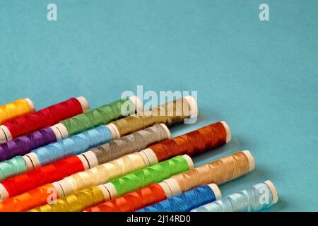 Spools of colored thread lie diagonally in the lower left corner on a light blue background Stock Photo