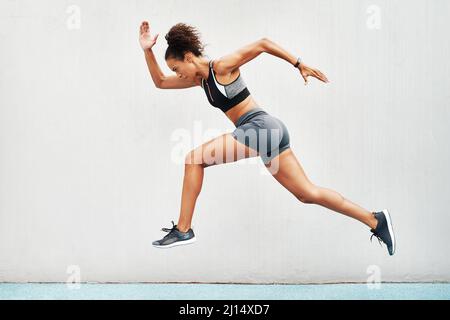 As we run, we become. Full length shot of an attractive young athlete jumping while on a track field during an outdoor workout session. Stock Photo