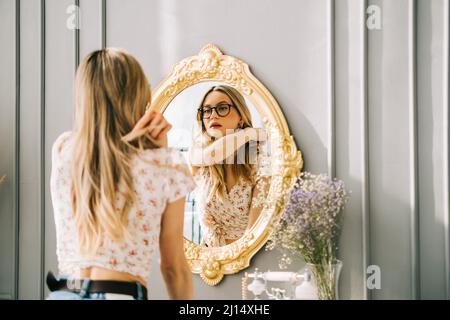 Young attractive caucasian woman looking in the mirror at her face, beauty treatment, skin care concept. Stock Photo