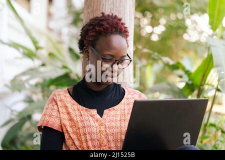 Beautiful Female African Student,wearing glasses,working on her Laptop in the University Garden. Stock Photo