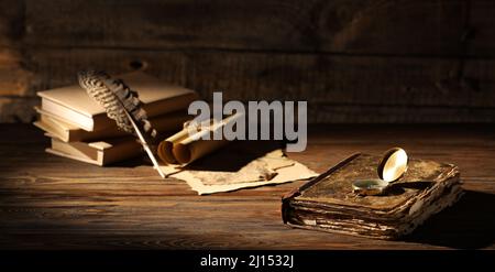 Old books with compass, feather and scrolls on wooden table Stock Photo