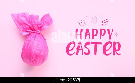 Chocolate egg wrapped in pink paper and text HAPPY EASTER on color background Stock Photo