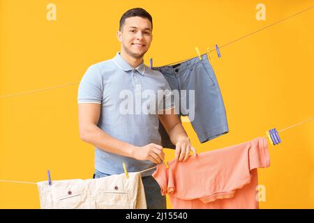 Young man hanging clean t-shirt with plastic clothespin on yellow background Stock Photo