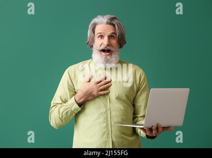 Surprised senior man with laptop on green background Stock Photo