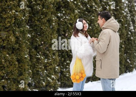 Loving couple with oranges in string bag holding hands on snowy winter day Stock Photo