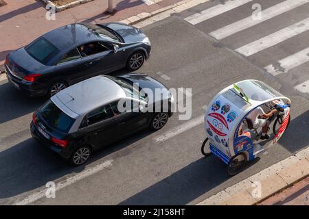 Nice, France - August 13, 2018: Cars and tourists trishaw bike are on the road on a sunny day