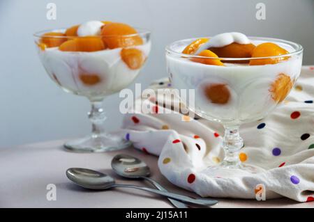 Peach slices dipped in yogurt with a little on a slice in the center, make up the image two spoons and a colored cloth the background is shaded and ou Stock Photo