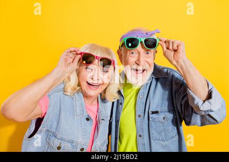 Portrait of attractive amazed cheerful grey-haired family touching specs having fun isolated over bright yellow color background Stock Photo
