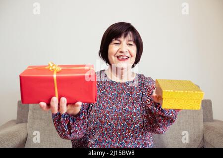A grandma holds a red and a yellow present on her hands at home Stock Photo