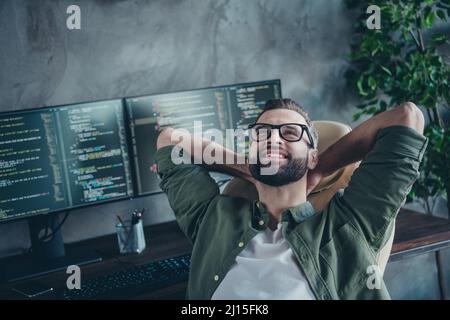 Photo of clever dreamy man wear green shirt spectacles having rest after developing software hands behind head indoors workshop workplace Stock Photo