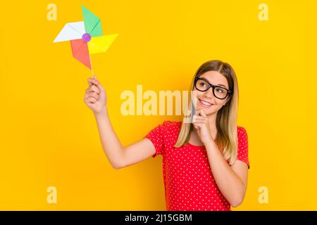 Photo of youth lovely girl have fun hand touch chin hold origami eyewear isolated over yellow color background Stock Photo