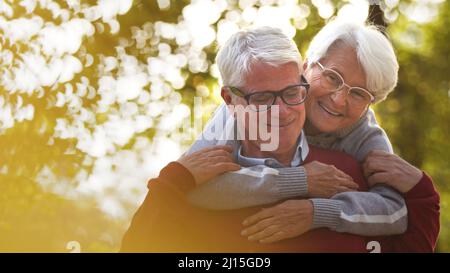 Portrait of happy elderly Caucasian couple woman hugs her husband from the back both smiling man looking down, woman looks away selective focus . High quality photo Stock Photo