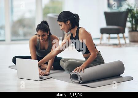 Lets start our virtual session. Shot of two young women using a laptop while working out at home. Stock Photo