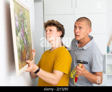 Son helps father to hang the painting on the wall of house Stock Photo