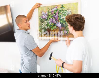 Son helps father to hang the painting on the wall of house Stock Photo