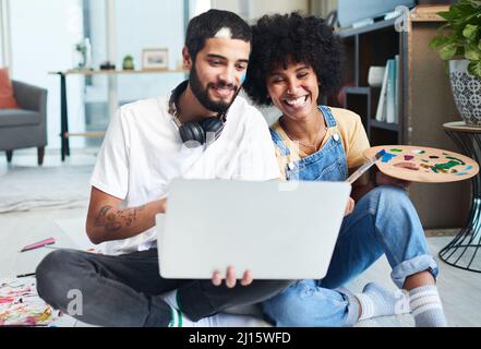 The internet is full of fun activities for couples. Shot of a young couple using a laptop while painting at home. Stock Photo