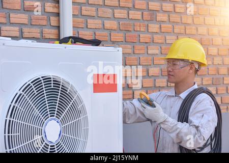 A young Asian air conditioner technician or air-conditioning installation technician is about to repair air conditioning in homes and buildings.Air co Stock Photo