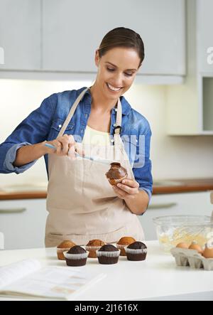Putting its the icing on the cupcake. A happy young woman about to apply frosting to her freshly-baked batch of cupcakes. Stock Photo