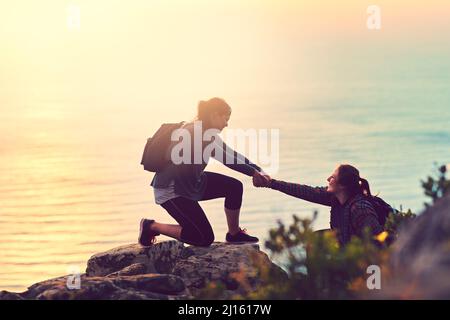 The best view comes after the hardest climb. Shot of a young woman helping her friend up a mountain. Stock Photo