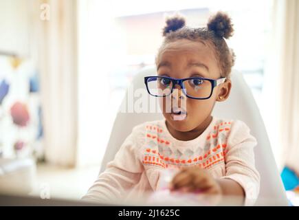 Oops.... Cropped portrait of an adorable little girl looking shocked while sitting down at home. Stock Photo