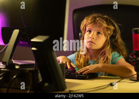 A little boy child uses a desktop at night, a child with computer screen in the room with neon lightning. School, study, online learning concept. Stock Photo