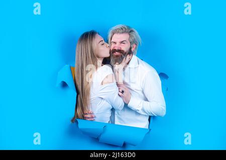 Couple through hole in blue paper, copy space for text or slogan. Discount and sale, people hole background. Surprised couple of bearded man and happy Stock Photo