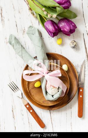 Easter table setting with painted eggs, purple tulip and cutlery on festive table. Table setting for Happy Easter day. Top view flat lay. Stock Photo