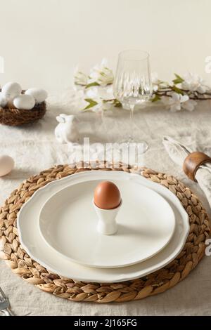 Easter table setting in festive morning with organic egg, spring blossom flowers on linen tablecloth. Vertical format. Close up. Stock Photo
