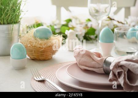 Easter table setting with blue eggs, spring decorations, fresh flowers. Elegance dinner in interior. Close up. Stock Photo