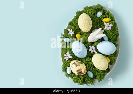 Easter DIY composition in plate for festive table set with rabbit, eggs, moss, and spring flowers on blue background. Banner. Greeting card. Copy spac Stock Photo
