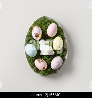 Easter composition in plate with rabbit, moss and craft eggs decorated gold foil on gray background. Greeting card. Concept Easter eggs hunt. DIY. Squ Stock Photo