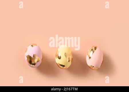 Three colorful eggs decorated gold foil on pink background. Happy Easter greeting card with copy space. Top view. Stock Photo