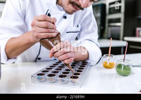 young latin man chocolatier in chef hat standing with mexican chocolates candies on plate in a commercial kitchen in Mexico Latin America Stock Photo