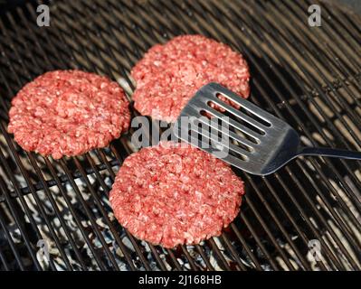 top view of raw beef hamburger patties on barbecue grill grate with spatula Stock Photo
