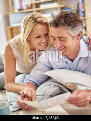 Taking a trip down memory lane. Shot of a smiling mature couple lying on their living room floor looking at photographs. Stock Photo