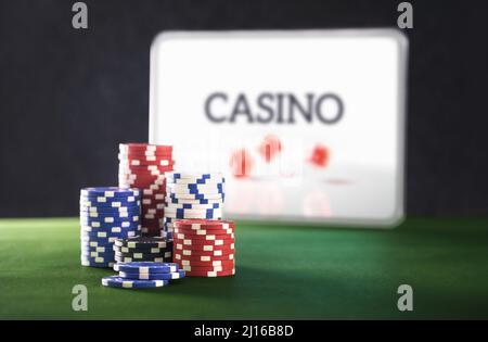 Gambling on internet casino. Online betting with tablet, computer or laptop. Stack of poker chips on green table. Playing digital mobile games. Stock Photo