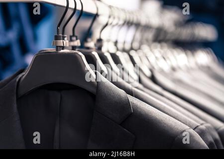 Suits in fashion store for men or in hanger in wardrobe. Jacket rack in apparel retail shop. New elegant luxury collection. Stock Photo