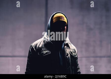Hooded criminal in dark. Mystery man with hood. Gangster in urban street. Hooligan in hoodie. Stalker with hidden face. Unknown suspicious thief. Stock Photo