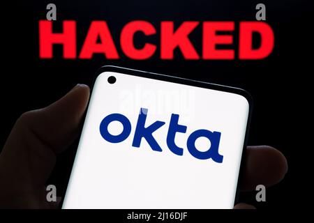 Okta security firm logo seen on smartphone and the word HACKED on blurred background. Concept for hack. Stafford, United Kingdom, March 22, 2022. Stock Photo