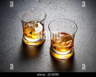 Two glasses of elegant whiskey with ice on black textured background. Hard drink concept. Stock Photo