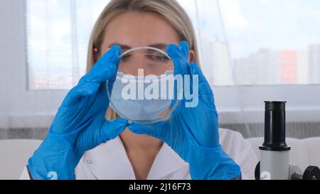 Female laboratory assistant analyzes samples using a microscope while working at a table in a laboratory, doing research Stock Photo