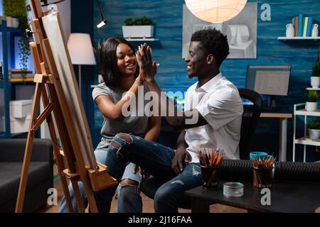Young man artist giving high five to collegue after finished drawing vase illustration on canvas working with professional painting tools. Designer team sketching masterprice using graphic pencil Stock Photo
