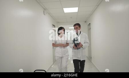 Two doctors walk down corridor and discussing about mri brain scan. Healthcare professional looking x-ray of patient's walking along corridor of Stock Photo
