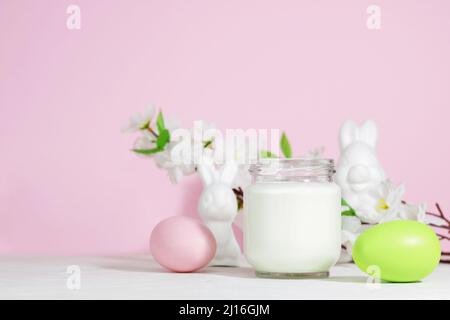 Organic probiotic milk kefir drink or yogurt in a glass container, with colored Easter eggs, on a pink background with a rabbit. Easter concept. Cold Stock Photo