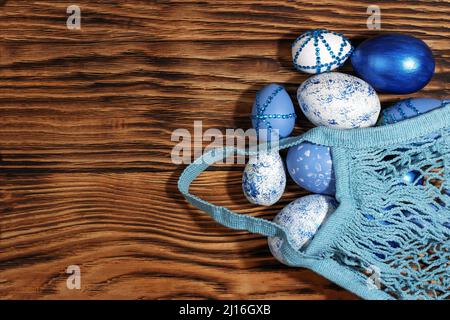 Blue, white, with rhinestones Easter eggs in a string bag on a trendy yellow wooden background. The minimal concept of Easter. Top view. Easter card w Stock Photo